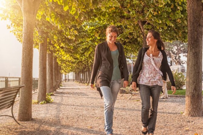 Zwei Frauen gehen zusammen im Park spazieren, umgeben von Bäumen. Entspannte Mittagspause im Tagesablauf mit Keto