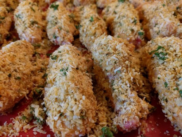 Frisch panierte ketogene Chicken Wings mit Parmesanpanade, bereit zum Backen auf einem mit Backpapier ausgelegten Blech.