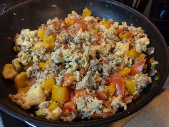 Frische Eier, Hackfleisch, Tomaten und Paprika braten in einer Pfanne mit goldbraunen Pinienkernen – ein schnelles Keto Frühstück in Zubereitung.  