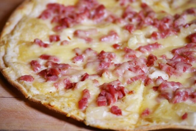 Nahaufnahme eines knusprigen Keto Flammkuchens mit geschmolzenem Käse und Speck auf einem Holzbrett