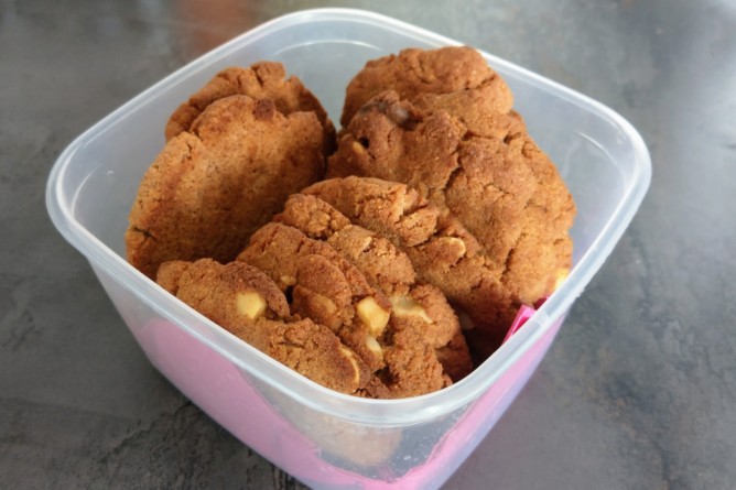 Frisch gebackene ketogene Macadamia White Chocolate Cookies in einer Dose gestapelt, goldbraun mit sichtbaren Nüssen und Schokoladenstückchen.  